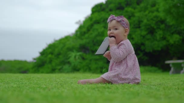 야외에서 검은 스마트폰을 씹고 빨고 있는 6 개월된 귀여운 여아의 모습. — 비디오