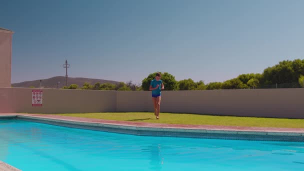 Νεαρό αγόρι που τρέχει την ημέρα και πηδάει στο νερό της πισίνας. — Αρχείο Βίντεο