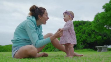 Bebek çimenlerde ilk adımı atıyor. Anne, kızıyla birlikte doğa çocuğunun rüya konseptinde yürüyor. Bebek annesiyle ilk adımı atıyor. Anne ve küçük kızı yakın çekim mutlu aile.