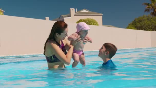 Famille relaxante dans la piscine extérieure. Garçon sautant dans la piscine et éclaboussant l'eau sur maman et petite soeur se baignant. Plaisir d'été. — Video