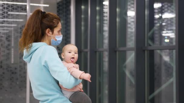 Une mère avec un masque médical tient une petite fille dans ses bras à l'aéroport dans la zone de départ. — Video