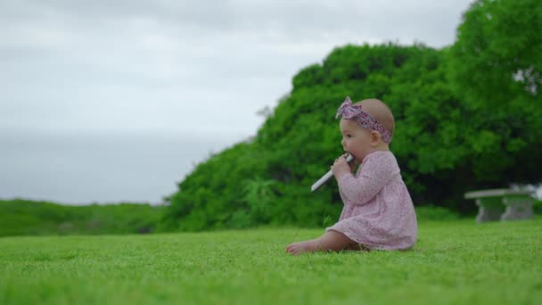 Retrato de adorable niña de 6 meses que está masticando y chupando el teléfono inteligente negro en el exterior. — Vídeo de stock