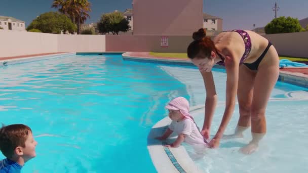 Aile yüzme havuzunun dışında dinleniyor. Çocuk havuza atlıyor ve annesinin ve küçük kız kardeşinin üzerine su sıçratıyordu. Yaz eğlencesi. — Stok video