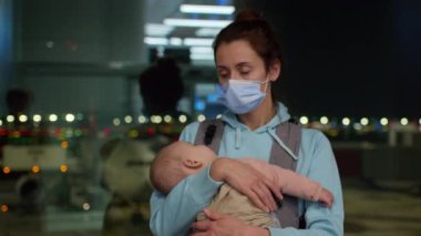 Tıbbi maskeli bir anne, ayrılış bölgesindeki havaalanında küçük bir kızı kollarında tutuyor..