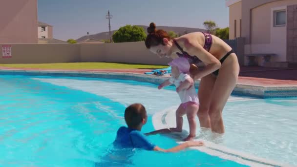 Famille relaxante dans la piscine extérieure. Garçon sautant dans la piscine et éclaboussant l'eau sur maman et petite soeur se baignant. Plaisir d'été. — Video