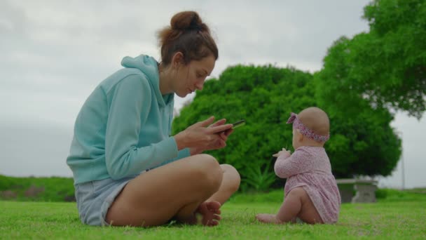 Γυναίκα με τηλέφωνο για μωρά. Όμορφη μητέρα με το μωρό αναζητούν smartphone. Σύγχρονη μαμά με παιδί κρατώντας κινητό στο χέρι εξωτερική. — Αρχείο Βίντεο