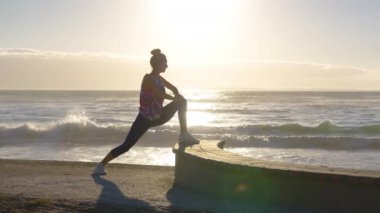 Spor kadını silueti, sabah sahilde ve denizde ısınma egzersizi yapıyor. Aktif kadın güneş doğarken spor yapıyor..