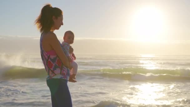 Mãe e bebê bonito no pôr do sol perto do oceano. Família feliz mãe e filha. — Vídeo de Stock