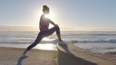 Spor kadını silueti, sabah sahilde ve denizde ısınma egzersizi yapıyor. Aktif kadın güneş doğarken spor yapıyor..
