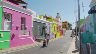 Bo-Kaap Cape Town Güney Afrika 'daki renkli binaların caddelerinde oğlu ve bebek arabasıyla yürüyen bir kadın..