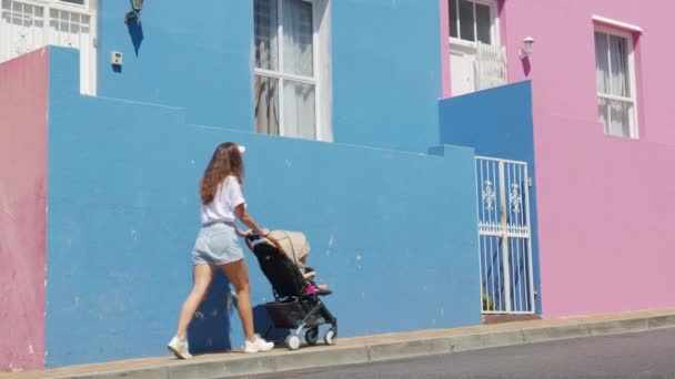 Женщина, прогуливающаяся с детской коляской по улицам красочных зданий района Бо-Каап Кейптаун Южная Африка. — стоковое видео