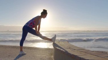 Spor kadını silueti, sabah sahilde ve denizde ısınma egzersizi yapıyor. Aktif kadın güneş doğarken spor yapıyor..