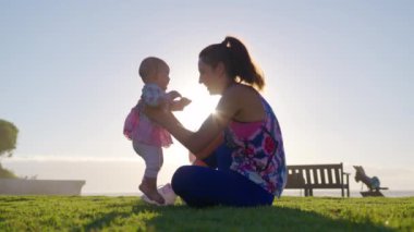 Genç anne, gün batımında bir okyanus sahilinde tatil sırasında kollarını tutuyor ve küçük bir kızla oynuyor..