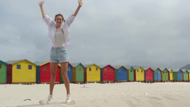 Een meisje dansen op het witte zand van Zuid-Afrika in de buurt van het kleurrijke bos Muizenberg Beach Houses. — Stockvideo