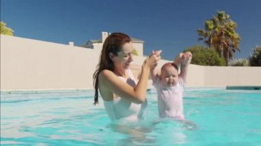 Sevimli küçük bebek ve annesi havuzda yüzme dersi alıyorlar. Anne bebeği elinde tutuyor ve ona sarılıyor..