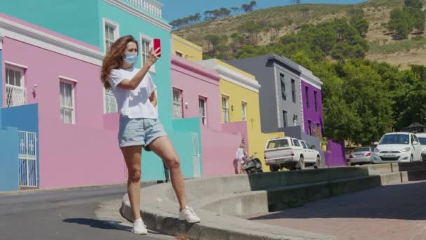 Mulher turista em tiros pandêmicos ao telefone na cidade do Cabo Bo-Kaap área malaia, perspectiva de rua pedra calçada, casas de terraço coloridas, África do Sul. — Vídeo de Stock