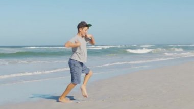 Sahilde dans eden komik çocuk. Eğlenceli ve pozitif duygu yavaşlığı çekiyor. Gülen erkek çocuk tatilde deniz kıyısında rahatlarken dans gösterisi yapıyor..