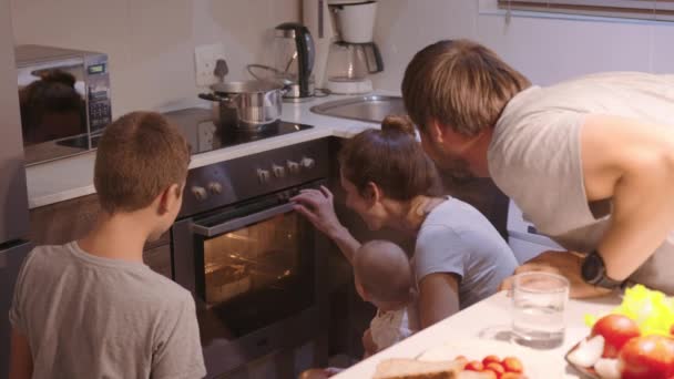 Die Familie schaut zu, wie ein Kuchen im Ofen zubereitet wird. Glückliche Kindheit. Gemeinsam hausgemachtes Essen zubereiten. — Stockvideo