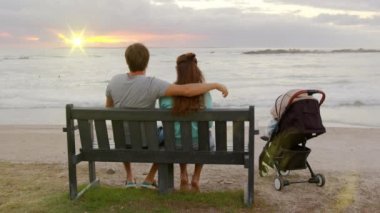 Okyanusun kenarında bebek arabasıyla gün batımını seyreden sevgi dolu bir çift..