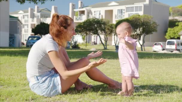 Gelukkige moeders en baby op een wandeling in het park. Mooi klein meisje staat op met moeder ondersteuning. Leren lopen met je moeder. Eerste stap in het leven. — Stockvideo