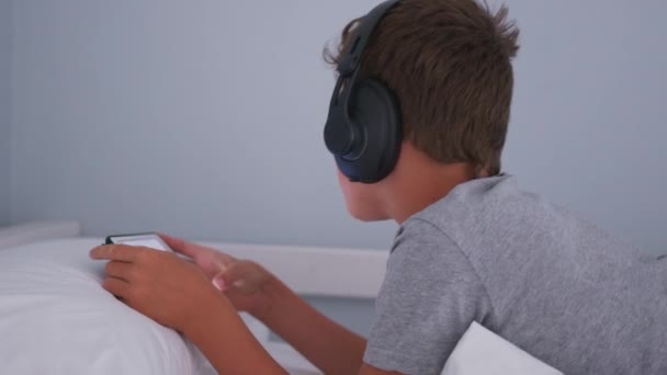 Adolescente en auriculares escuchando música mientras mira la tableta en su habitación. — Vídeos de Stock