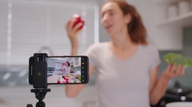 Sevimli bir kadın mutfağın içinde yemek pişirme videosu kaydediyor. Güzel genç bayan blogcu sağlıklı yemek hazırlarken taze organik sebze kullanıyor..