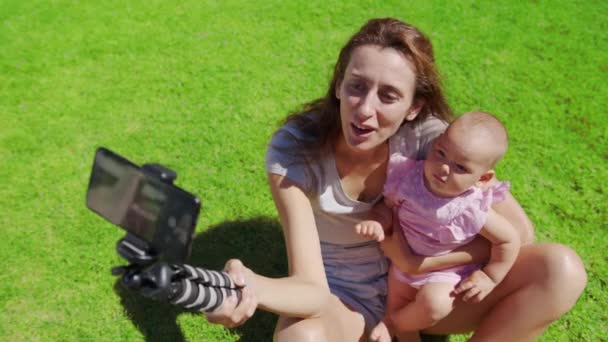 Madre blogger con hija pequeña divirtiéndose graba un video blog sobre hierba verde. — Vídeo de stock