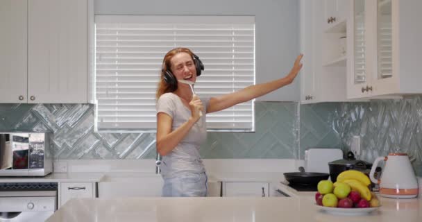 Retrato de mujer alegre cantando canción en bigote en cocina domética en cámara lenta. Chica positiva divirtiéndose con utensilio de cocina en casa. Mujer joven bailando en la cocina. — Vídeo de stock