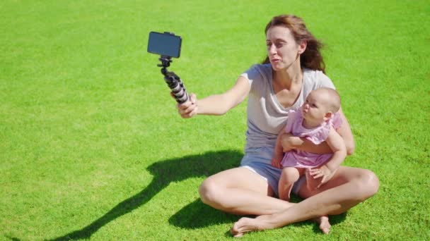 Madre blogger con hija pequeña divirtiéndose graba un video blog sobre hierba verde. — Vídeo de stock