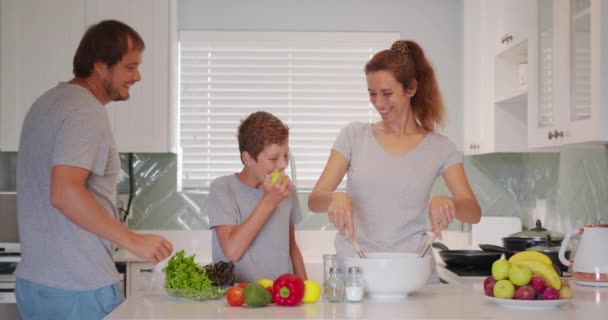 In de keuken: moeder, vader en schattig jongetje samen koken Gezond eten. Ouders leren Little Son Healthy Habits en hoe groenten te mengen in de salade Bowl. Schattig kind helpt zijn ouders. — Stockvideo