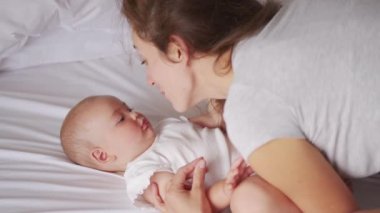 Sevgi dolu genç bir anne, tatlı tatlı tatlı bir kızı kucaklayarak yatakta yatıyor. Gülümseyen anne ve yatak odasında kucaklaşan sevimli küçük kız çocuğu. Anne ve çocuğun hassas anları.