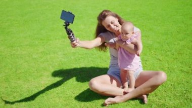 Küçük kızı olan anne blogcu yeşil çimenler üzerine bir video blogu kaydediyor..