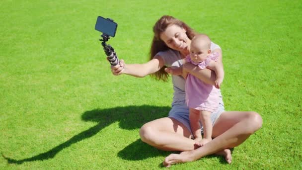 Madre blogger con hija pequeña divirtiéndose graba un video blog sobre hierba verde. — Vídeo de stock