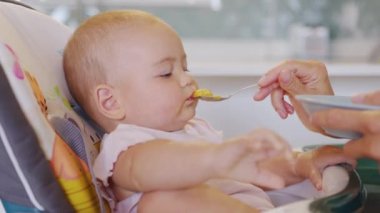 Kadın çocuğu kaşıkla besliyor. Anne bebeği püre yiyecekle besliyor. Anne, bebek koltuğundaki çocuğu besliyor..
