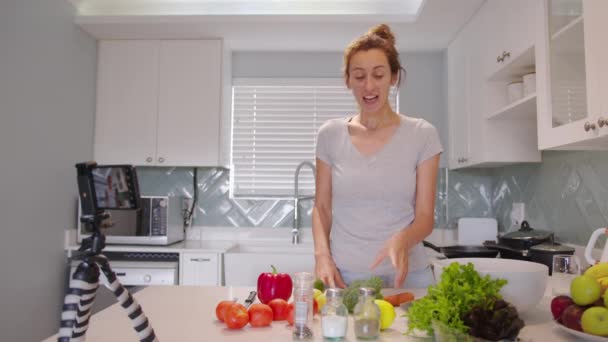 Красивая женщина говорит запись кулинарного видео в кухонном интерьере. Красивая молодая женщина-блоггер готовит здоровую пищу, используя свежие органические овощи. — стоковое видео