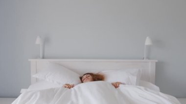 A woman sleeped in bed under a white blanket and afraid, frightened. Fright.