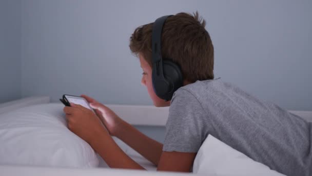 Adolescente em fones de ouvido ouvindo música enquanto olha para o tablet em seu quarto. — Vídeo de Stock