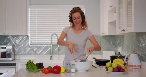 Portrait of cheerful woman singing song in whisker on domestic kitchen in slow motion. Positive girl having fun with kitchen utensil at home. Young woman dancing on kitchen. — Wideo stockowe