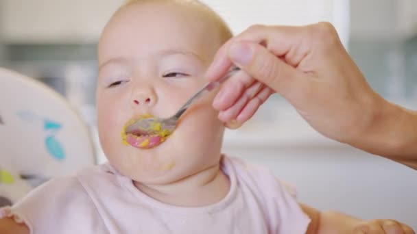 Woman feeding child with spoon. Mom feed baby with pureed food. Mom feeding kid in baby chair. Closeup. — Stock Video