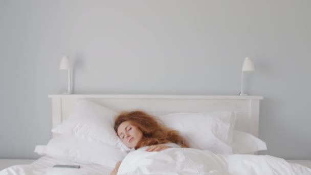 Close-up shot van slaperige blanke vrouw wakker in de ochtend, het nemen van smartphone en het uitschakelen van de wekker om meer slaap te krijgen. — Stockvideo