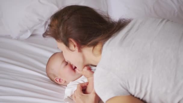 Houden van jonge mama knuffelen rustgevende schattige lieve baby meisje liggend in bed. Lachende zorgzame moeder en schattig klein kind meisje knuffelen in de slaapkamer. Moeder- en kindgevoelige momenten. — Stockvideo