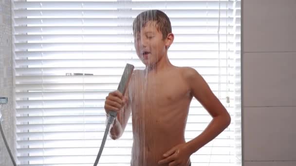 Joyeux garçon chantant et dansant tout en prenant une douche dans la salle de bain. — Video