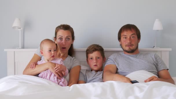 Vrolijke jonge Europese familie met twee kinderen komen samen op de bank om TV te kijken in de badroom glimlachend. Samenzijn en vermaak. — Stockvideo