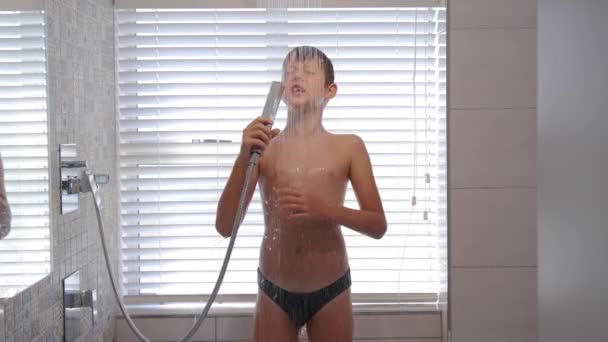 Jonge jongen neemt een douche en zingt emotioneel als in een microfoon. Waterstralen stromen door het gezicht en de borst. — Stockvideo