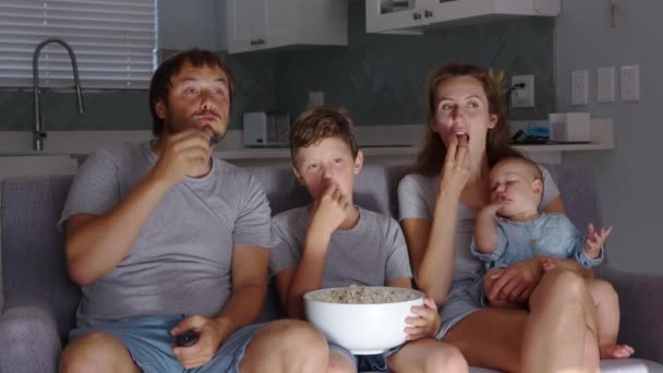 Joyeux jeune famille européenne avec deux enfants se réunissent sur le canapé pour regarder la télévision à la maison souriant. Ensemble et divertissement. — Video