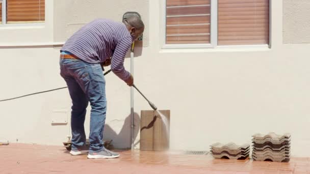 Tegola di pulizia con rondella di pressione dell'acqua. Janitor spruzza strada marciapiede della città pavimentazione lastre. L'uomo nero disinfetta pavimento e superfici da coronavirus. Misure sanitarie antibatteriche sulla quarantena. — Video Stock