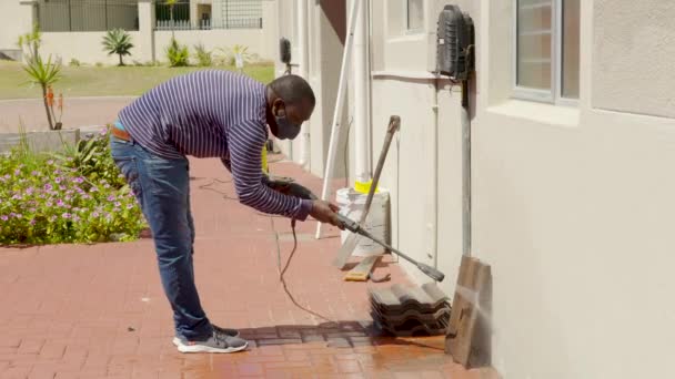 Limpieza de baldosas con lavadora a presión de agua. El conserje rocía la acera de la ciudad pavimentando losas. El hombre negro desinfecta el suelo y las superficies del coronavirus. Medidas sanitarias antibacterianas en cuarentena. — Vídeo de stock