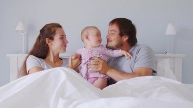 Genç aile, baba, anne ve bebek birlikte gülüyor, sarılıyor, yatakta uzanıyor. Beyaz Ev İçi.