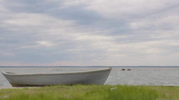 A wooden fishing boat moored on a sandy and grassy shore at sunset with a cloudy sky, time lapse. — Stock Video