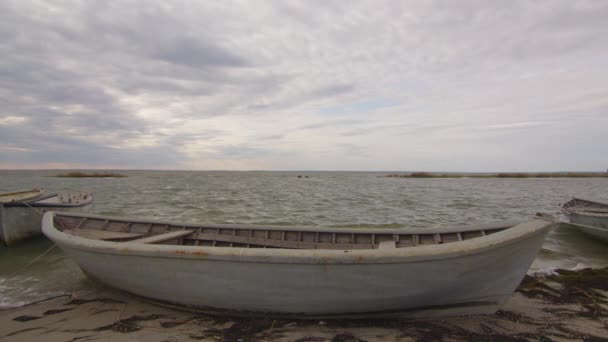 A wooden fishing boat moored on a sandy and grassy shore at sunset with a cloudy sky, time lapse. — Stock Video